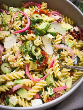 Epic Pasta Salad served in a bowl with fusilli, avocado, feta, olives, sundried tomatoes, herbs, pickled onions, and shaved parmesan.