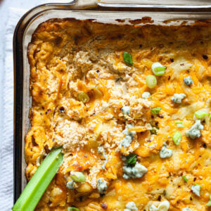 Close-up of buffalo chicken dip with a scoop taken out, showing creamy texture and a celery stick dipped into the hot, cheesy surface.