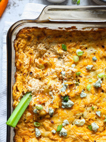 Close-up of buffalo chicken dip with a scoop taken out, showing creamy texture and a celery stick dipped into the hot, cheesy surface.