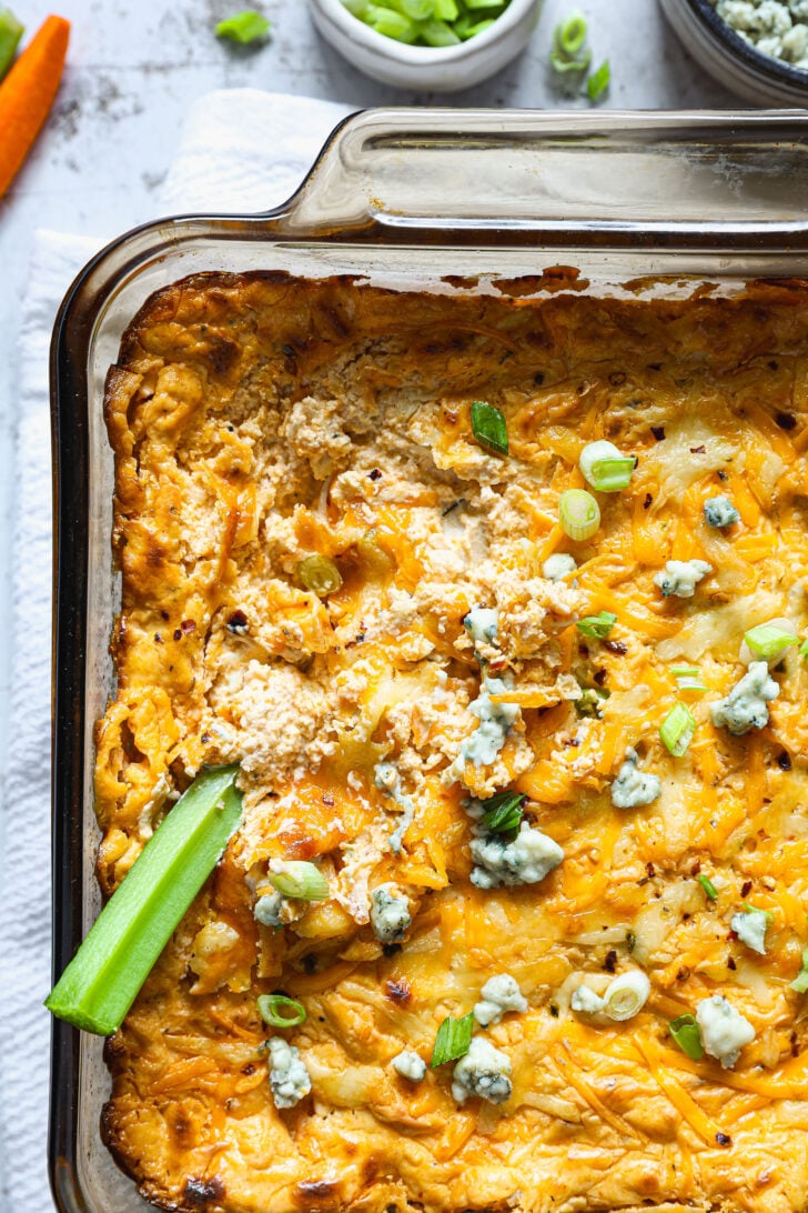 Close-up of buffalo chicken dip with a scoop taken out, showing creamy texture and a celery stick dipped into the hot, cheesy surface.