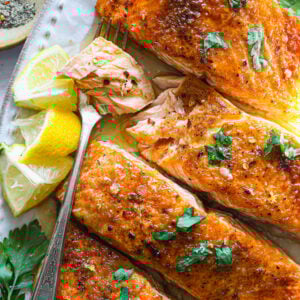 Fork-tender salmon flaked open to reveal juicy, glazed flesh, with lemon wedges and fresh parsley on a white serving plate.