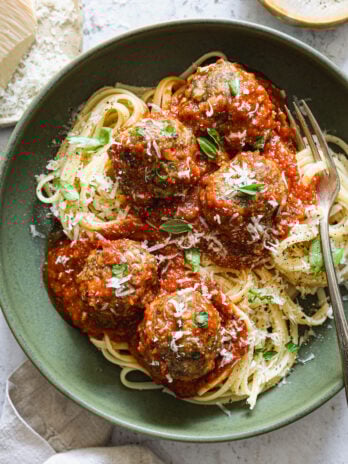 Plated spaghetti topped with tomato sauce, meatballs, fresh basil, and grated Parmesan, served in a green bowl with a fork.