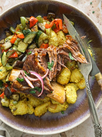 Plated braised short rib over mustard-curry gnocchi and roasted ratatouille, garnished with pickled shallots and herbs.