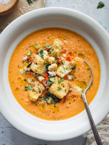 Finished bowl of gazpacho topped with croutons, diced vegetables, fresh herbs, cracked pepper, and a drizzle of olive oil.