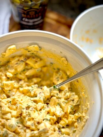 Fully assembled egg salad in a bowl showing creamy texture with visible chives, red onion, dill, and cornichon pieces.